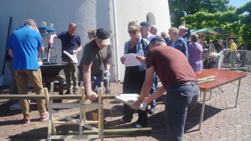 Buiten bij de molen. Een aantal mannen staan de heklatten van de molen te zagen