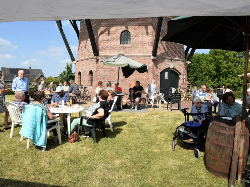 Mensen zitten op stoeltjes bij tafels gezellig voor de Puurveense molen. 