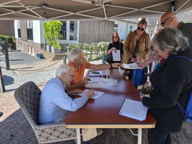 Groep mensen. twee mannen zitten aan een tafel en delen certificaten uit aan de bezoekers